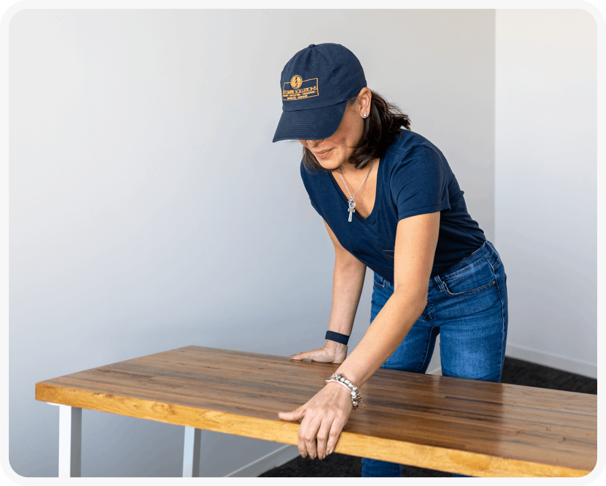 A woman in blue shirt and hat leaning on wooden table.
